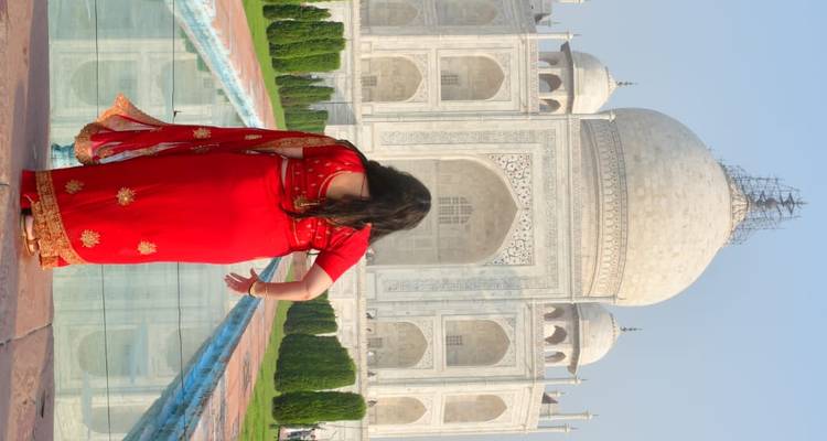 Een vrouw in een felrode sari kijkt naar de marmeren pracht van de Taj Mahal aan de overkant van de reflectievijver.