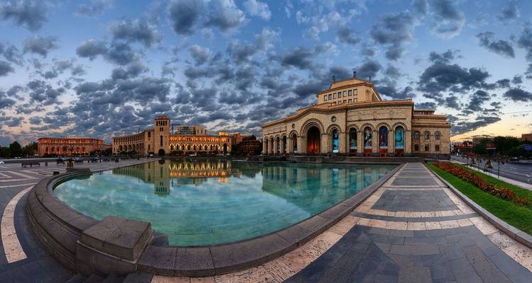 Spacious plaza with architectural buildings and a reflection pool at dusk.