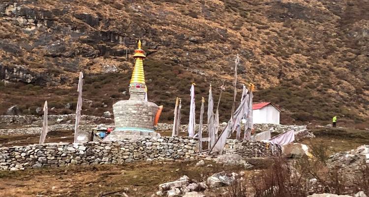 Un stupa entouré de rochers et de drapeaux de prière dans une région montagneuse.