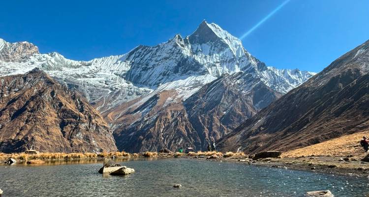 Pristine alpine pool mirrors a dramatic snow-covered Himalayan peak under a dazzling blue sky.