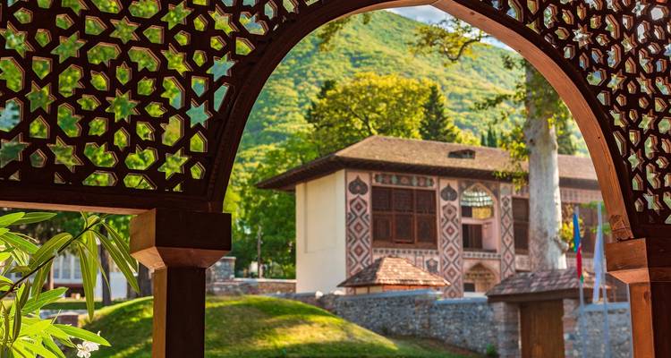 Decorative archway leading to a historic building in a lush setting.