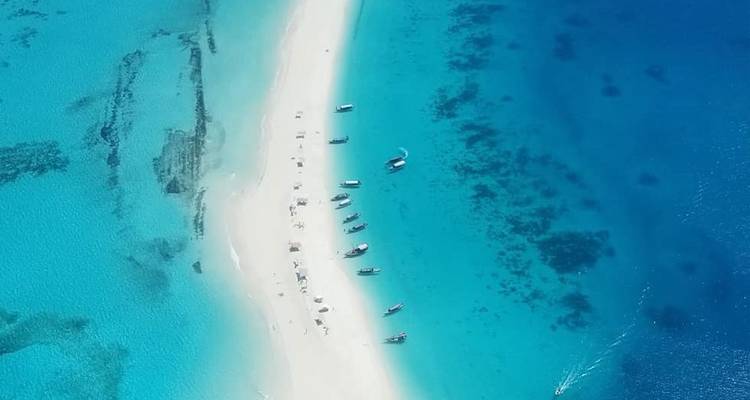 Vista aérea de una barra de arena blanca rodeada de aguas turquesas vibrantes salpicadas de pequeños botes.