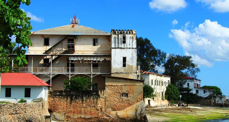 Edificio histórico desgastado por el tiempo encaramado en la costa de Zanzíbar bajo un cielo azul brillante.