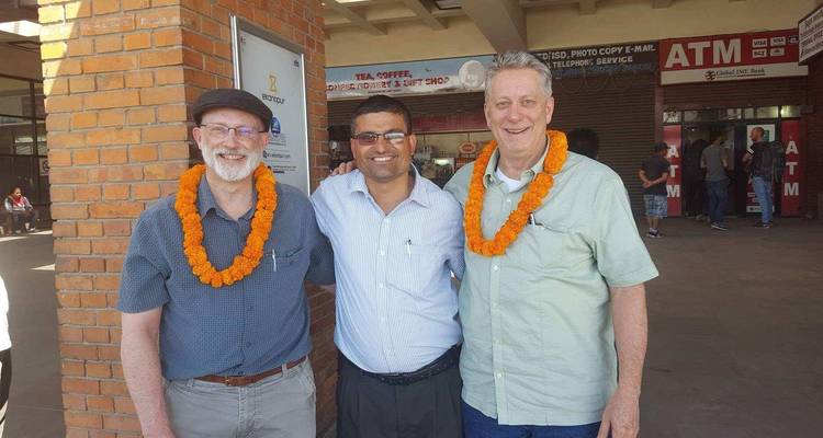 Tres hombres usando guirnaldas parados frente a un edificio de ladrillo.