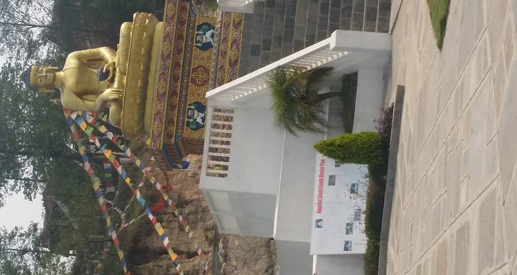 Estatua dorada de Buda con banderas de oración y escalones.