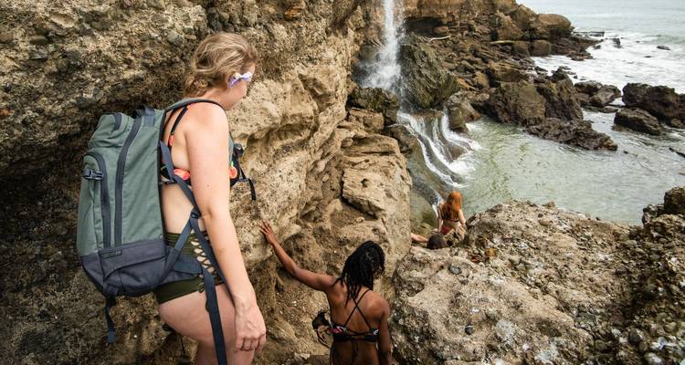Women climbing up rocks near a small waterfall.