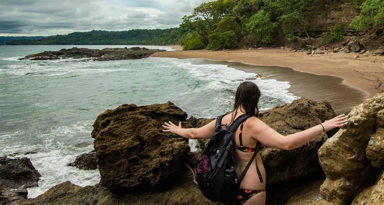 Woman standing on rocks overlooking a beach.