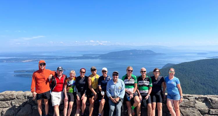 Gruppe posiert auf einer Steinmauer vor einer malerischen Landschaftskulisse.