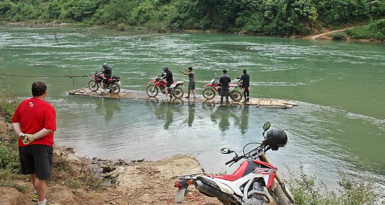 People transporting motorcycles on a bamboo raft across a river.