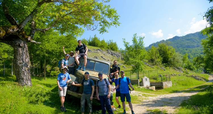 Group of people posing by an old vehicle in a rural setting.