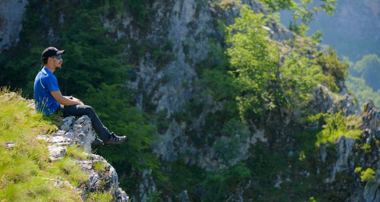 Man sitting on a rock in a mountainous landscape.