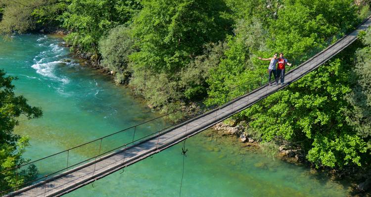 Two people posing on a narrow suspension bridge over turquoise water.