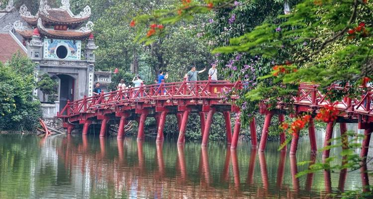 Un puente de madera rojo sobre un lago tranquilo con personas caminando por él.