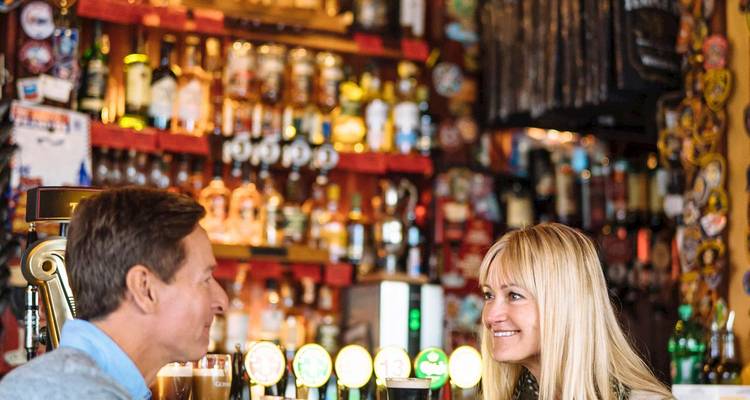 Repeat: happy couple enjoying drinks in a lively Irish bar with shelves of spirits behind them.