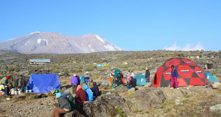 Wanderer versammelten sich in einem Basislager mit Zelten in einer felsigen Landschaft.