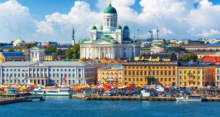 Vista del paseo marítimo de la Plaza del Senado de Helsinki con la catedral de cúpula blanca dominando los coloridos edificios del mercado y las barcas en el puerto en un día soleado y brillante.