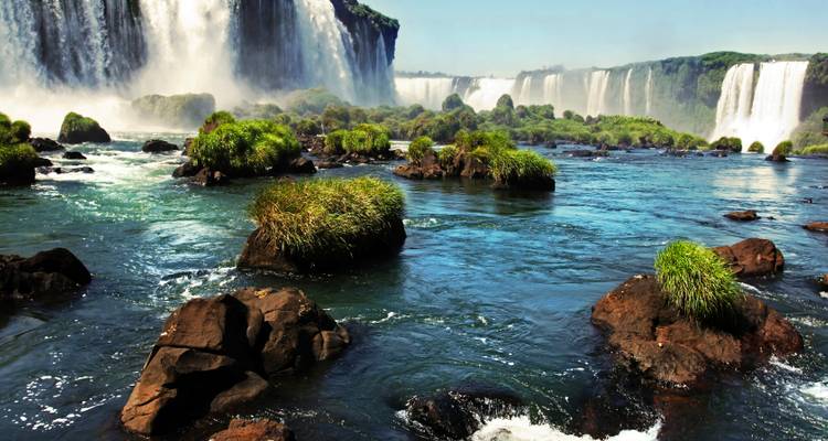 Vista desde el nivel del río de las Cataratas del Iguazú con islotes rocosos y exuberante vegetación rodeando las poderosas cascadas.