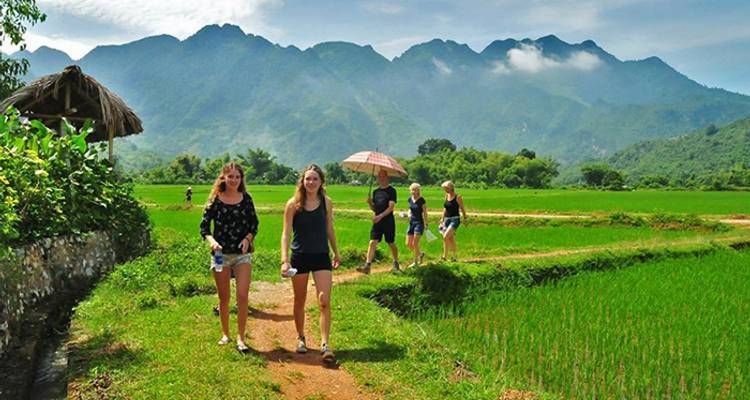 Turistas caminando por un sendero entre campos verdes y montañas