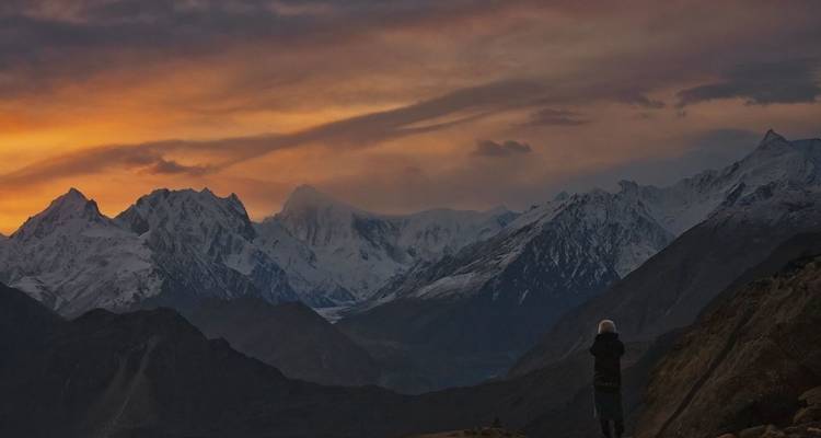 Personne regardant le coucher de soleil avec les montagnes en arrière-plan.