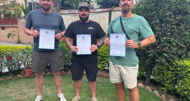 Tres hombres sosteniendo certificados, de pie en un área de jardín.