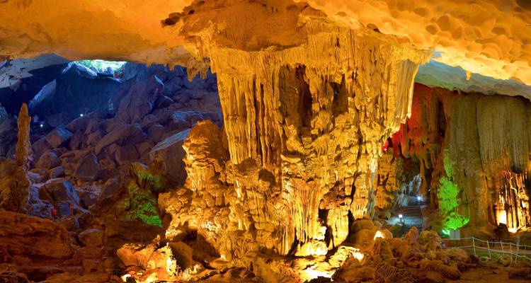 Colorfully lit cave interior with stalagmites and stalactites.