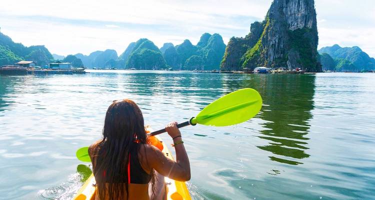 Person kayaking in Halong Bay with limestone formations in the background.