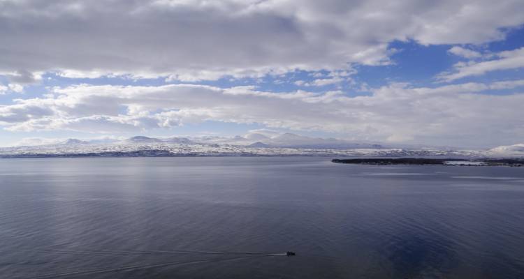 Friedlicher See mit schneebedeckten Bergen, die sich im Wasser spiegeln.