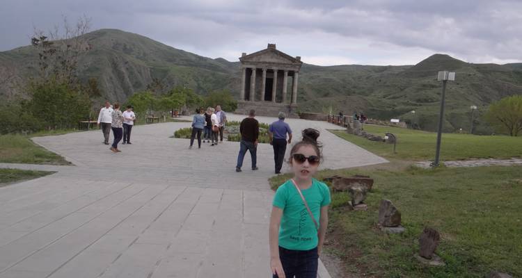 Touristen in der Nähe eines antiken Tempels vor bergiger Kulisse.