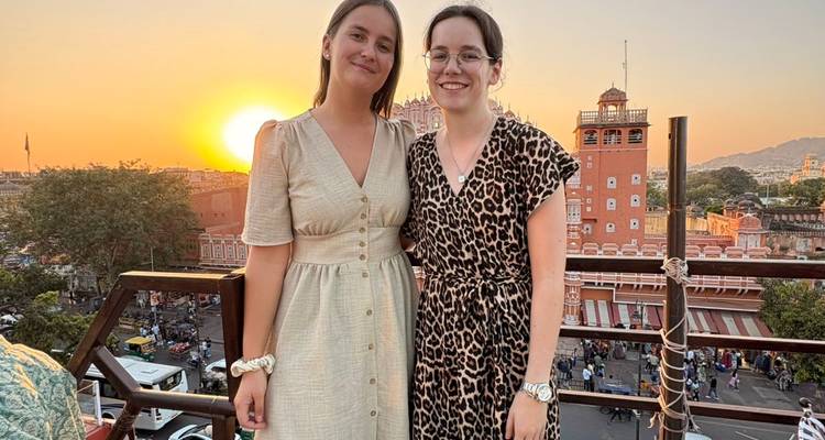 Twee mensen die staan met een zonsondergang en historische architectuur op de achtergrond.