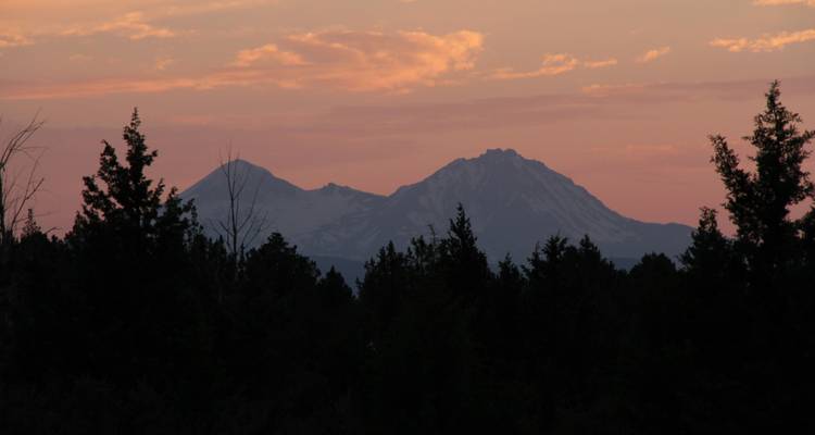 Silhouette de montagnes au coucher du soleil avec des arbres au premier plan.