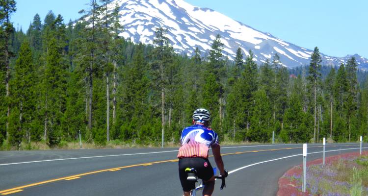 Cycliste sur une route avec une montagne enneigée en arrière-plan.