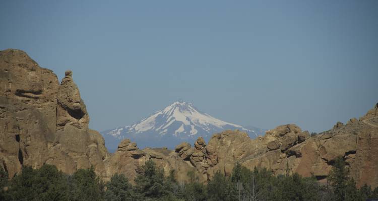 Montagne enneigée visible entre les formations rocheuses et les arbres.