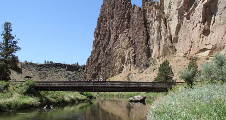 Des gens debout sur un pont au-dessus d'une rivière, avec des falaises rocheuses en arrière-plan.