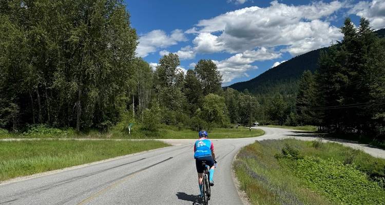 Radfahrer auf einer kurvenreichen Straße, umgeben von Wald.