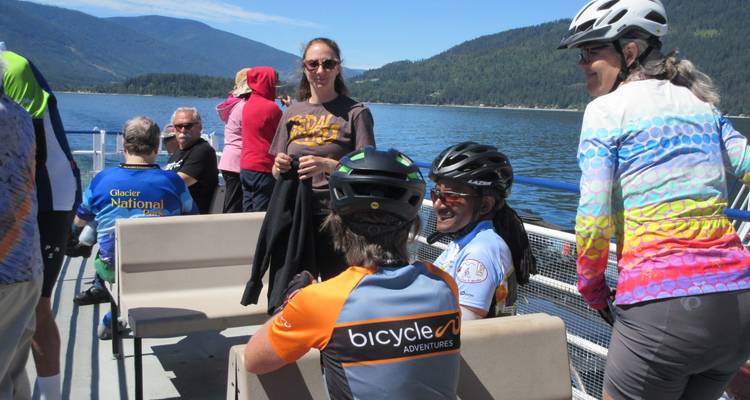 Gruppe von Menschen auf einer Fähre mit Bergen im Hintergrund.