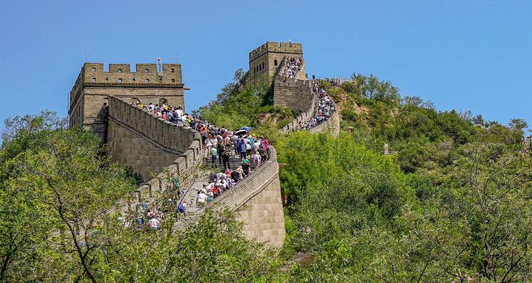 Une longue file de touristes monte une section escarpée de la Grande Muraille sous un ciel bleu dégagé