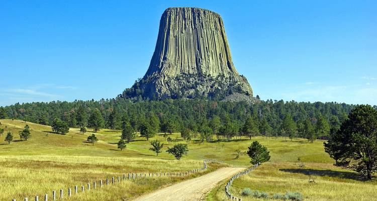 Formation rocheuse de Devils Tower avec un sentier qui y mène, entourée de prairies.