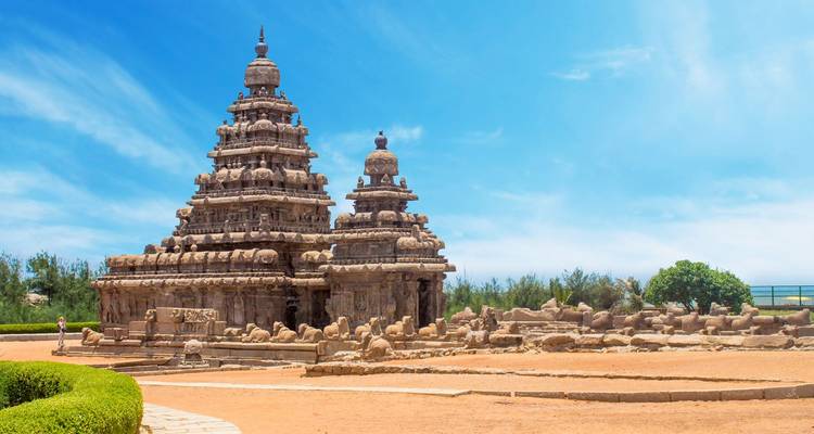 El Templo de la Orilla de Mahabalipuram enmarcado por un vibrante cielo azul y primer plano arenoso.