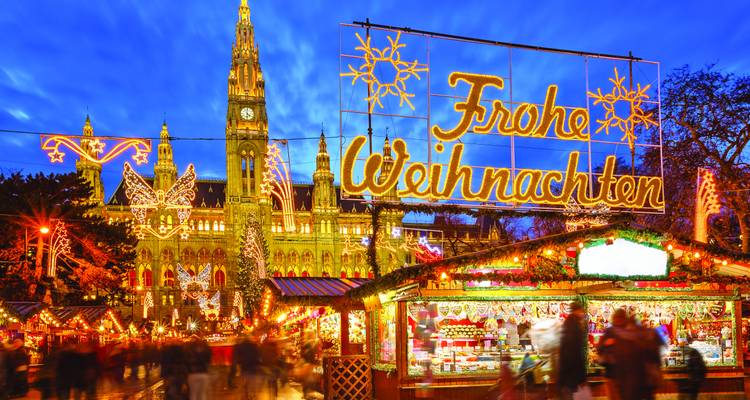 Vienna’s festive Rathausplatz glowing with ‘Frohe Weihnachten’ lights above bustling Christmas market stalls at dusk.