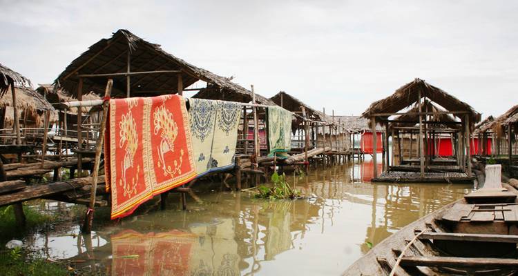 Des huttes rustiques sur pilotis avec des tapis colorés séchant au-dessus d'une eau boueuse dans un village flottant cambodgien.