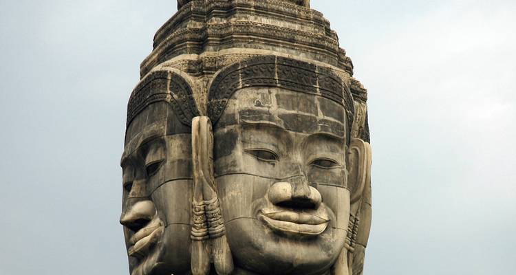 Gros plan des visages de pierre sérènes du Temple de Bayon sur un ciel pâle.