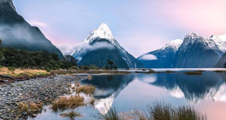 Fjord cristallin et calme reflétant les pics enneigés et le ciel pastel de l'aube à Milford Sound.