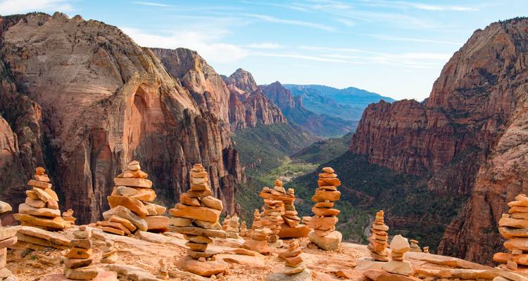 Gestapelte Steinpyramiden säumen einen Aussichtspunkt am Klippenrand mit Blick auf dramatische Sandsteinwände und ein tiefes Tal im Zion-Nationalpark.