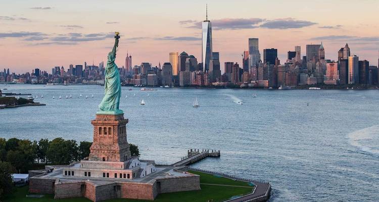La Statue de la Liberté surplombe le port de New York avec l'horizon de Manhattan qui brille au crépuscule