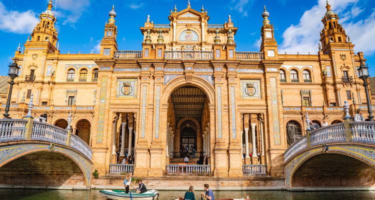 Großer zentraler Pavillon der Plaza de España in Sevilla, der sich in seinem Kanal spiegelt, mit Besuchern, die unter verzierten Brücken Boot fahren.