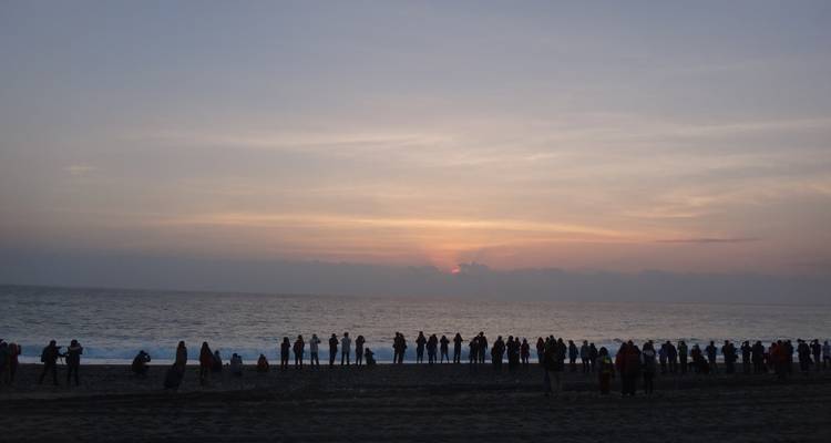 Sonnenuntergangsblick mit Menschen, die am Strand stehen und den Horizont beobachten.