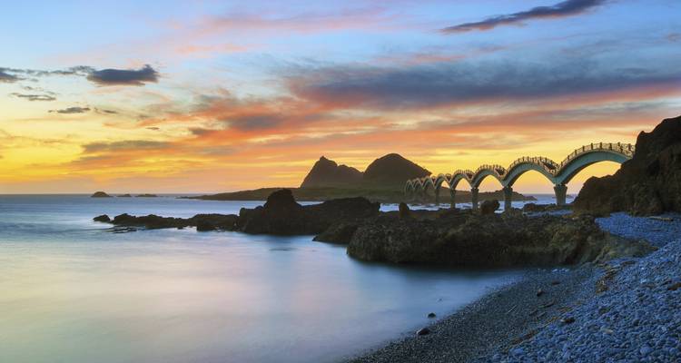 Vista del atardecer de costa rocosa con puente en arco.