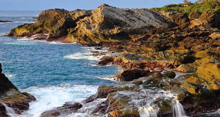 Costa rocosa con acantilados dentados y olas chocando contra piscinas de marea con la luz del amanecer.