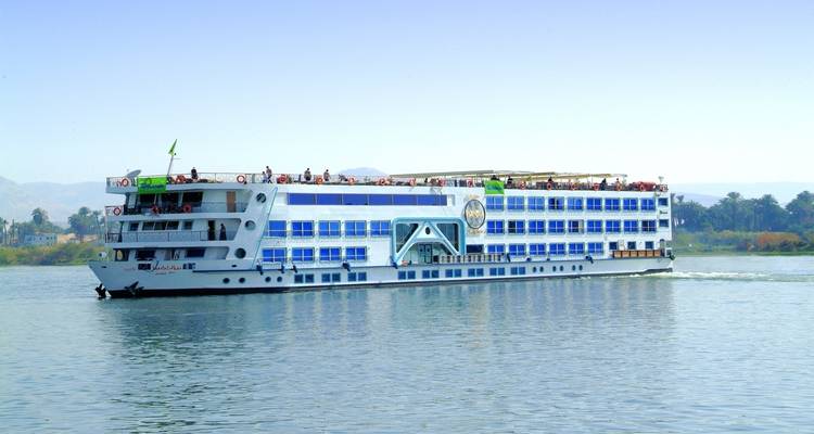 Un navire de croisière naviguant sur une rivière avec des palmiers et un paysage en arrière-plan.