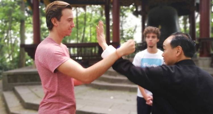 Young man learning tai chi with instructor and another person watching.
